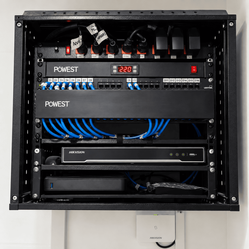 Rack de Ruedalar con panel de conexiones, cables de red azules y grabador de videovigilancia.