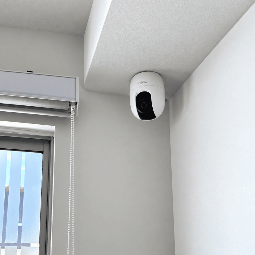 Cámara de seguridad interior instalada bajo una viga junto a una persiana.